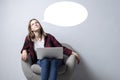 Young girl with a laptop sitting on a soft comfortable chair and thinking, a woman using a computer against a white blank wall, Royalty Free Stock Photo