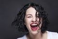 Young girl laughing contagiously with her mouth open. Beautiful bright curly brunette in a white tank top with red lipstick. Black Royalty Free Stock Photo