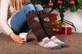 Young girl legs with warmers socks sitting on carpet floor and holding cup of coffee, Christmas tree and presents box in backgroun Royalty Free Stock Photo