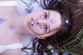 Young girl lies in hair tangled blue spring flowers