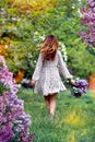 A young girl in a light dress, a view from the back, walking along the green grass with a bouquet of lilacs. Royalty Free Stock Photo