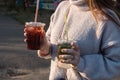 A young girl in a light sweater holds two cocktails in her hands in the rays of sunset Royalty Free Stock Photo