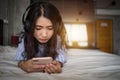 Young girl listening music from smartphone on bed at home. Asian woman lying on bed holding mobile phone listening music. Royalty Free Stock Photo