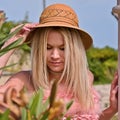 Young girl with long blond hair, crouching in a flower bed, wearing a sun hat Royalty Free Stock Photo