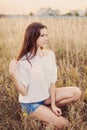 Young girl with long brown hair sitting in autumn field, smiling Royalty Free Stock Photo