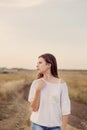 Young girl with long brown hair stays at the road in field