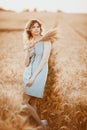 A young girl with long curly hair and a light blue dress , standing in a wheat field, against the background of the