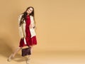 A young girl with long curly hair in a red dress and a white leather jacket with a bag in her hands on a pastel orange studio back Royalty Free Stock Photo