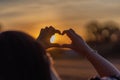 Young girl with long hair holding hands in the form of a heart against the backdrop of sunset, Poland Royalty Free Stock Photo