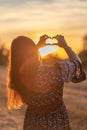 Young girl with long hair holding hands in the form of a heart against the backdrop of sunset, Poland Royalty Free Stock Photo