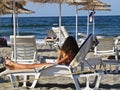 Young Girl with Long Hair Relaxing and Sitting on Beach Holding in Her Hand Mobile Smart Phone Reading Texting During Summer Royalty Free Stock Photo