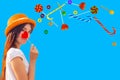 Young girl with long hair and a straw hat holds a lollipop of a heart shape and flying different sweets, copy space Royalty Free Stock Photo