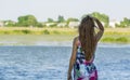 A young girl with long hair turned her back and stares into the distance on the river bank.