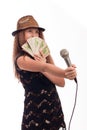 Young girl with long hair wearing a black dress and gold hat with a microphone in his hand and money on a white background Royalty Free Stock Photo