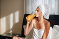 Young girl with long hair in white robe using laptop having breakfast orange juice in bed of hotel room. Lovely woman Royalty Free Stock Photo