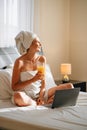 Young girl with long hair in white robe using laptop having breakfast orange juice in bed of hotel room. Lovely woman Royalty Free Stock Photo