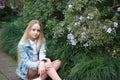 Girl with long white hair in a denim jacket walks in the garden with blooming azalea