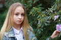 Girl with long white hair in a denim jacket walks in the garden with blooming azalea