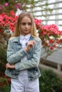 girl with long white hair in a denim jacket walks in the garden with blooming azalea