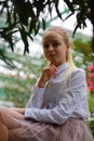 Young girl with long white hair in a white formal shirt and a short light skirt walks in the garden Royalty Free Stock Photo