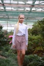 Young girl with long white hair in a white formal shirt and a short light skirt walks in the garden Royalty Free Stock Photo