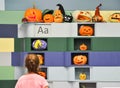 Young girl looking at the wall with various halloween carved orange pumpkins crafted by children at the education school