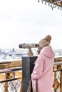 A young girl looks through coin-operated binoculars on the observation deck overlooking the city from a height at sunset. Winter,