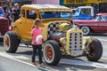 A young girl looks at the engine of a Ford Model A hot rod