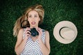 Young girl lying on the grass looking at the sky to take a photo with her camera, next to her is a hat Royalty Free Stock Photo