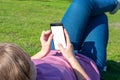 Young girl is lying on grass at the park on day off with cell pone on her hands. Woman