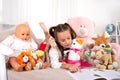 Young girl lying on the sofa at home and reading a book with her teddy bear and other toys around her