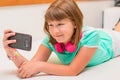 Young girl lying on sofa at home smiles with mobile phone in hand