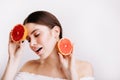 Young girl without makeup with clean soigne skin poses with red citrus fruits on white background. Royalty Free Stock Photo