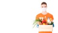 Young girl in a mask and an orange t-shirt holds a wooden box with groceries for delivery isolated on white background Royalty Free Stock Photo