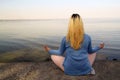 A young girl is meditating on the beach sitting on the shore