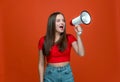 Young girl with megaphone announcing sale yelling at loudspeaker, black Friday shopping on orange studio background Royalty Free Stock Photo