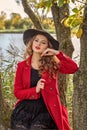 Girl model posing in a red coat and black hat on the branches of a tree on the river bank