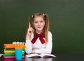 Young girl near empty green chalkboard showing finger up