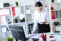 A young girl in the office is standing near the table, holding a pencil and a calculator in her hand and looking through Royalty Free Stock Photo