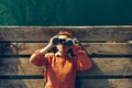 Young Girl Lies On A Pier Near The Sea And Looks Through Binoculars. Travel Search Journey Concept