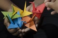 Holding Origami Paper Crane Orizuru in hand. Assorted Color Birds. on Black Background