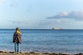 Young girl out of focus stood on beach looking out to sea in sunshine at big ocean liner oil tanker on the horizon Royalty Free Stock Photo