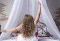 Young girl outstretching her arms sitting on the bed after good night sleep, back view Royalty Free Stock Photo