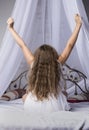 Young girl outstretching her arms sitting on the bed after good night sleep, back view Royalty Free Stock Photo