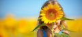 Young girl peeking behind sunflower in sunny field with blurred background, ideal for text