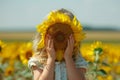 Young girl peeking behind sunflower in vibrant summer field, ideal for text, blurred background