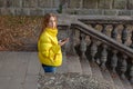 A young girl with phone, in yellow jacket, on the stairs of an old building. Autumn day. Royalty Free Stock Photo