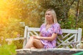 A young girl in a pink dress sits on a white wooden bench in the garden around flowers and plants with green leaves Royalty Free Stock Photo