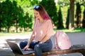 Young girl is studying in the spring park, sitting on the wooden bench and browsing on her laptop Royalty Free Stock Photo