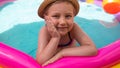 Young girl playing in colorful rainbow inflatable swimming pool.Child in straw hat and pink swimsuit in clear blue water.